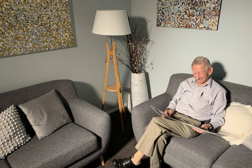 Ian sits on a couch smiling while looking at photos of his late relatives.