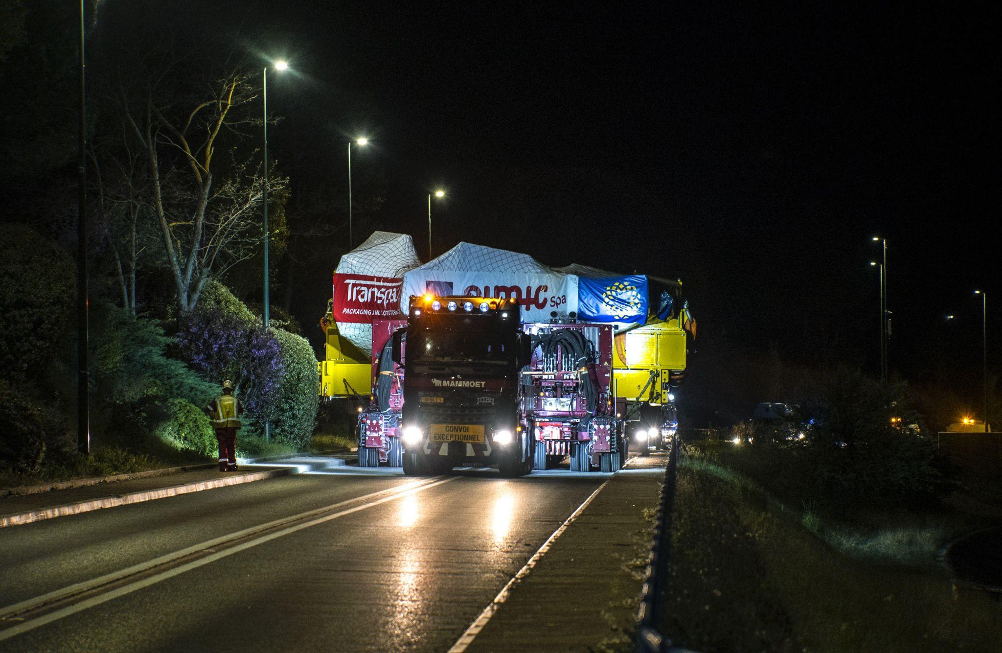 A truck hauls a massive component on a transportation bed that fills up both lanes of a highway
