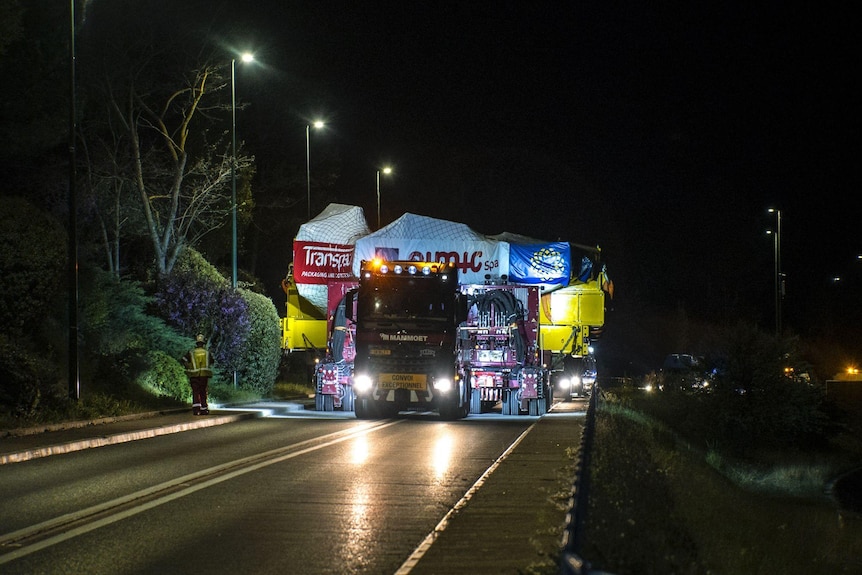 A truck hauls a massive component on a transportation bed that fills up both lanes of a highway