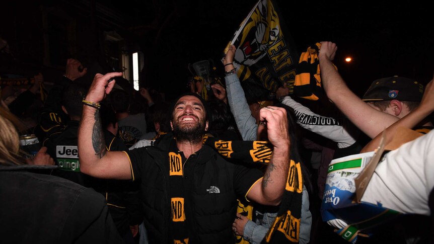 A man flexes his muscles and wears a richmond scarf in one of the busy pubs along the street.