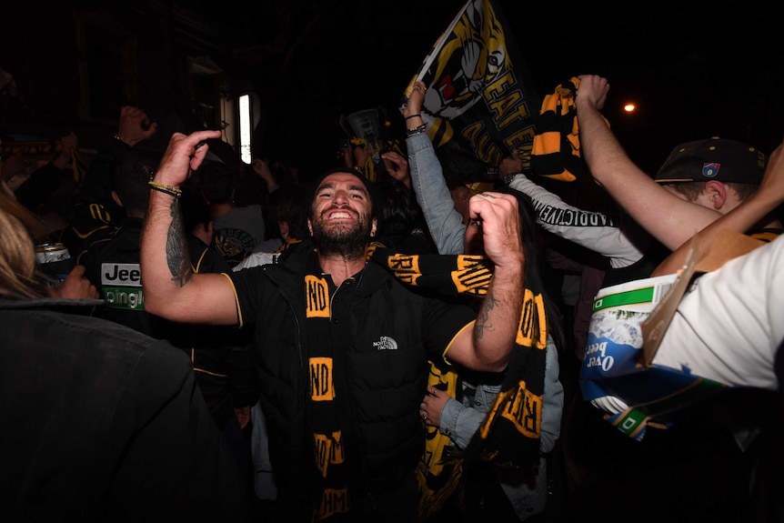 A man flexes his muscles and wears a richmond scarf in one of the busy pubs along the street.