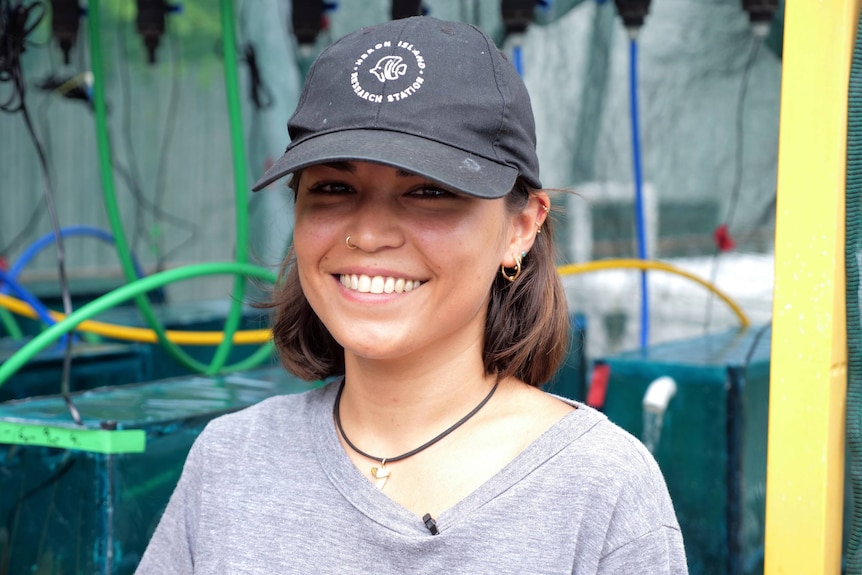 tight headshot of Morane smiling at the camera, wearing a cap, cords behind.