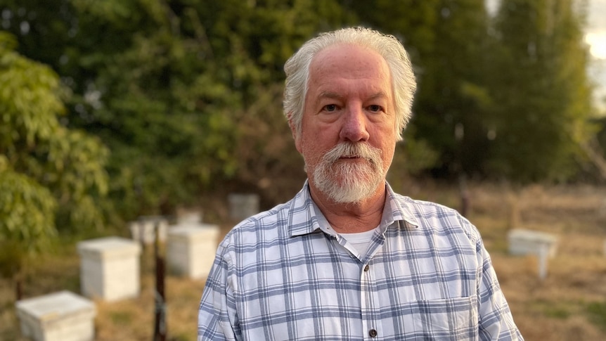 David Vial with a blank expression in front of his hives. 