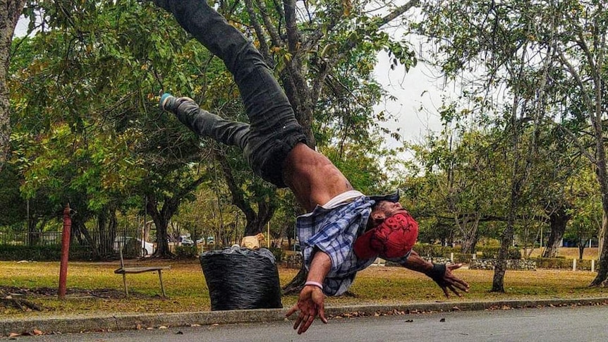 Man with red cap upside down, arms splayed, feet in the air.