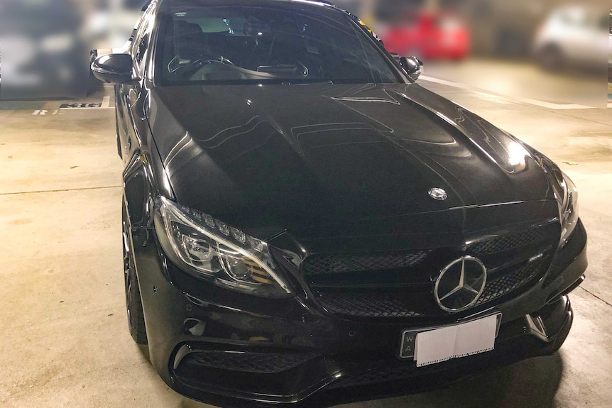 A front-on shot of a black Mercedes Benz sedan parked in an underground garage.