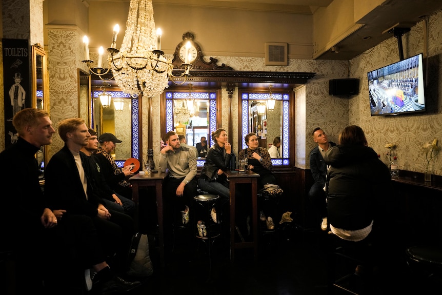 People sit and watch as the Queen's funeral plays on the TV. 