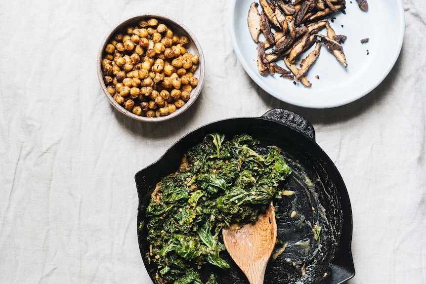 A bowl of crispy chickpeas, a plate of pan fried shiitake mushrooms and a cast iron skillet with creamed miso kale, for salad.