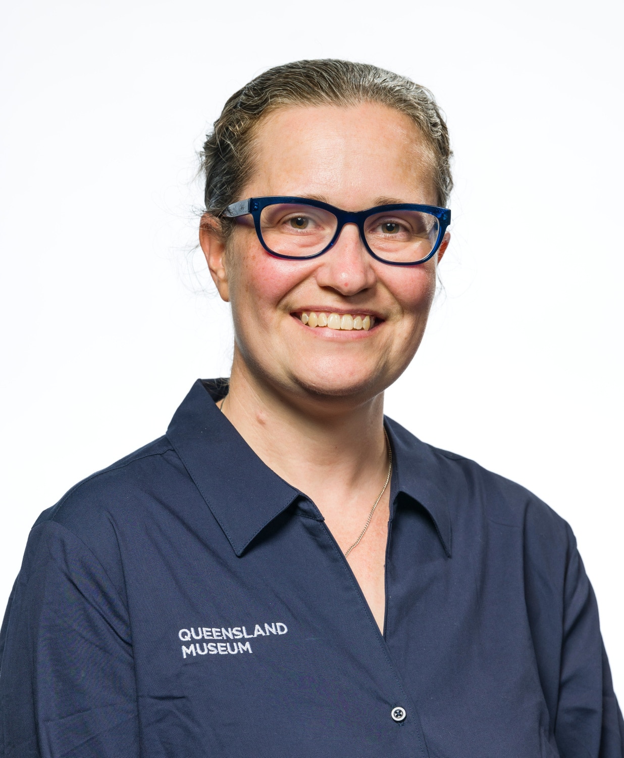 a woman wearing a Queensland Museum branded shirt smiles