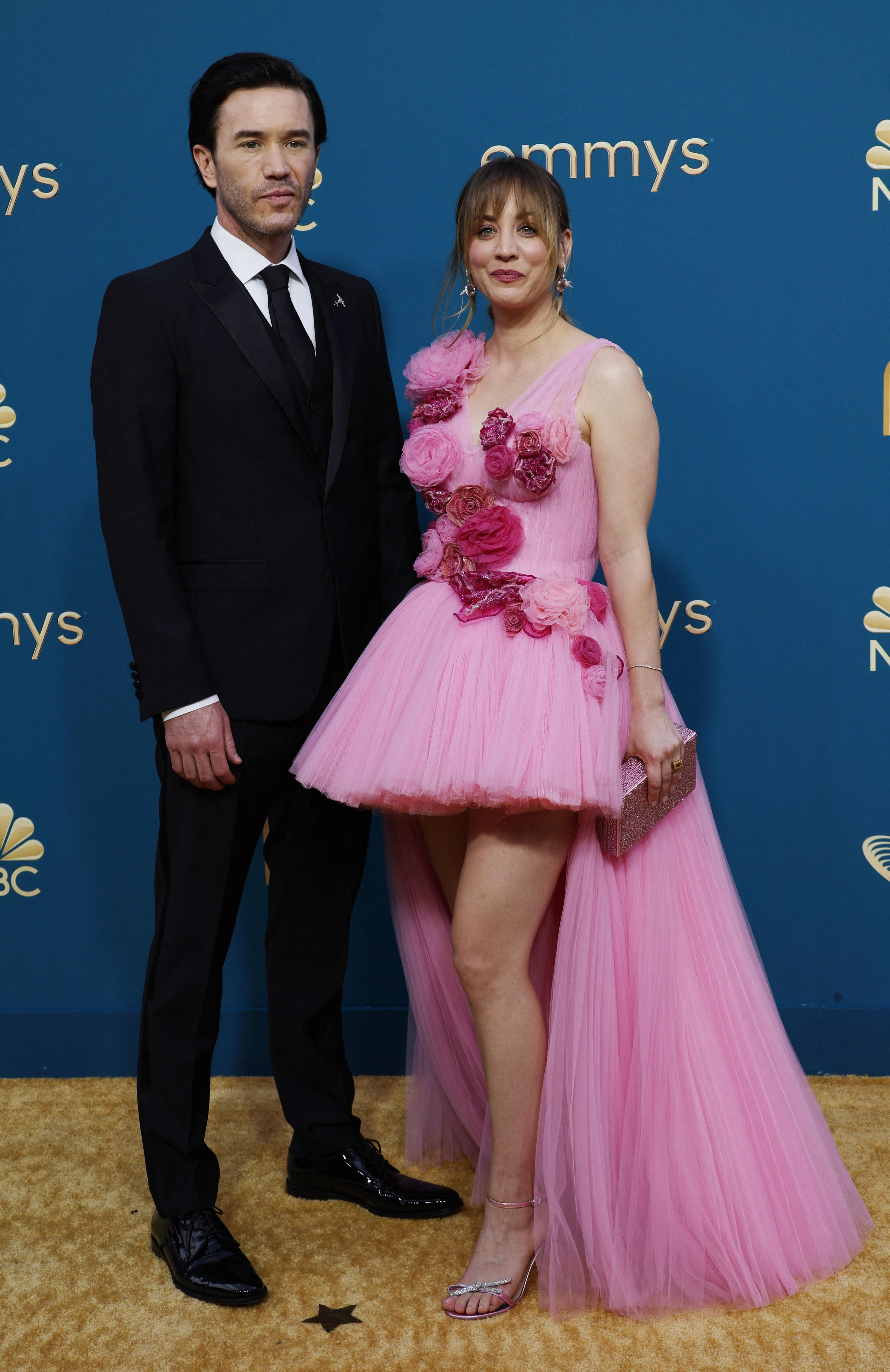 Tom Pelphrey wears a black suit and Kaley Cuoco wears a pink tulle dress with a short tutu-like skit and a floor-length train 