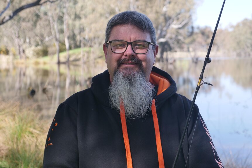 A man with glasses and a beard holding a fishing rod and smiling