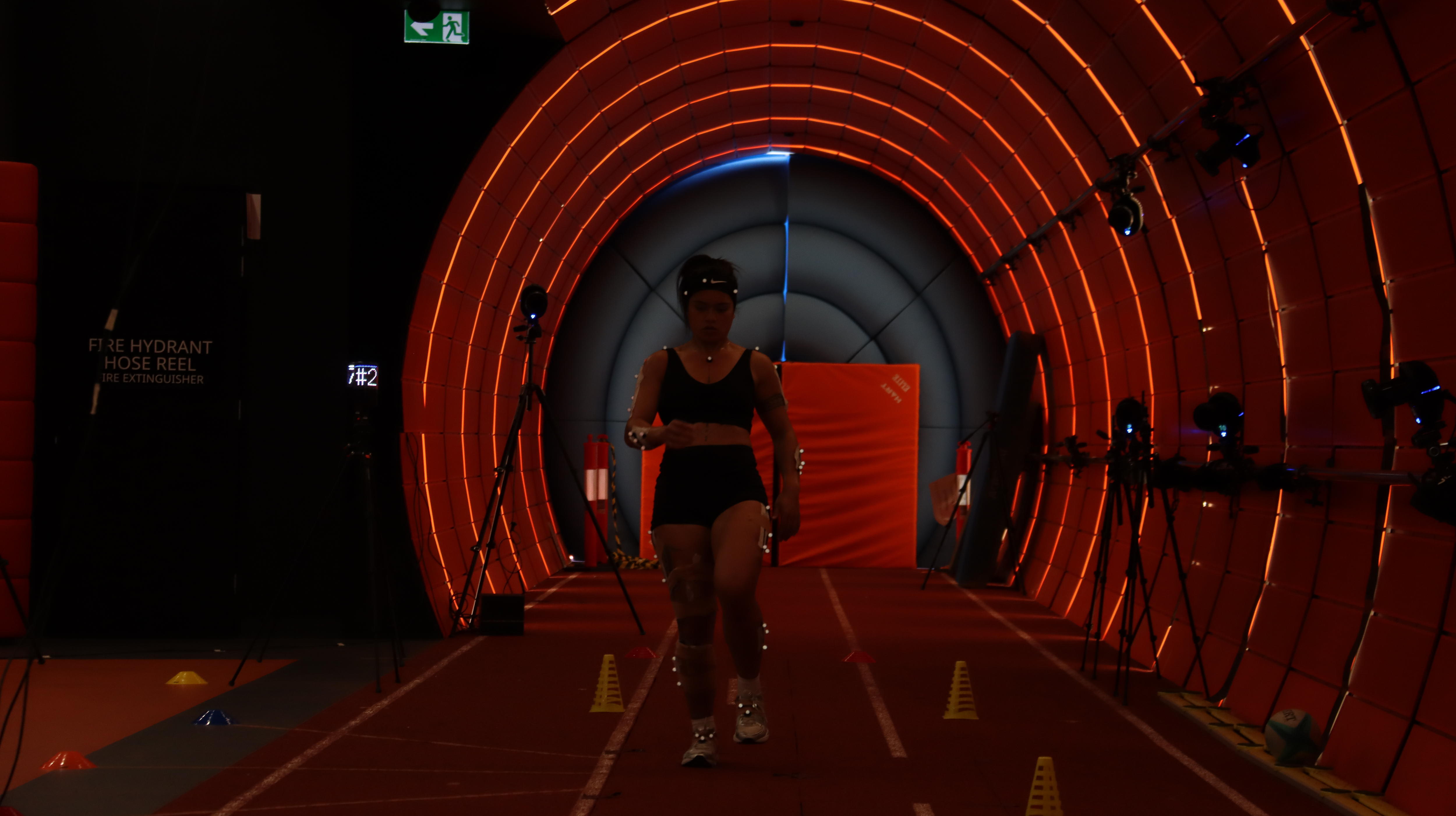 Una jugadora de rugby con luces de nudos en su cuerpo en una pista de pruebas cilíndrica de color naranja.