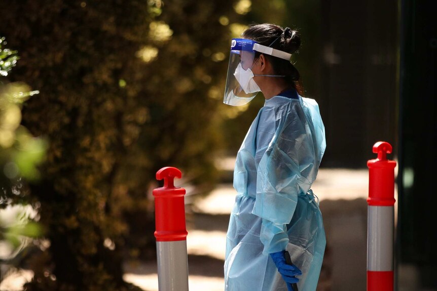 A woman dressed in PPE moves a luggage trolley at a quarantine hotel