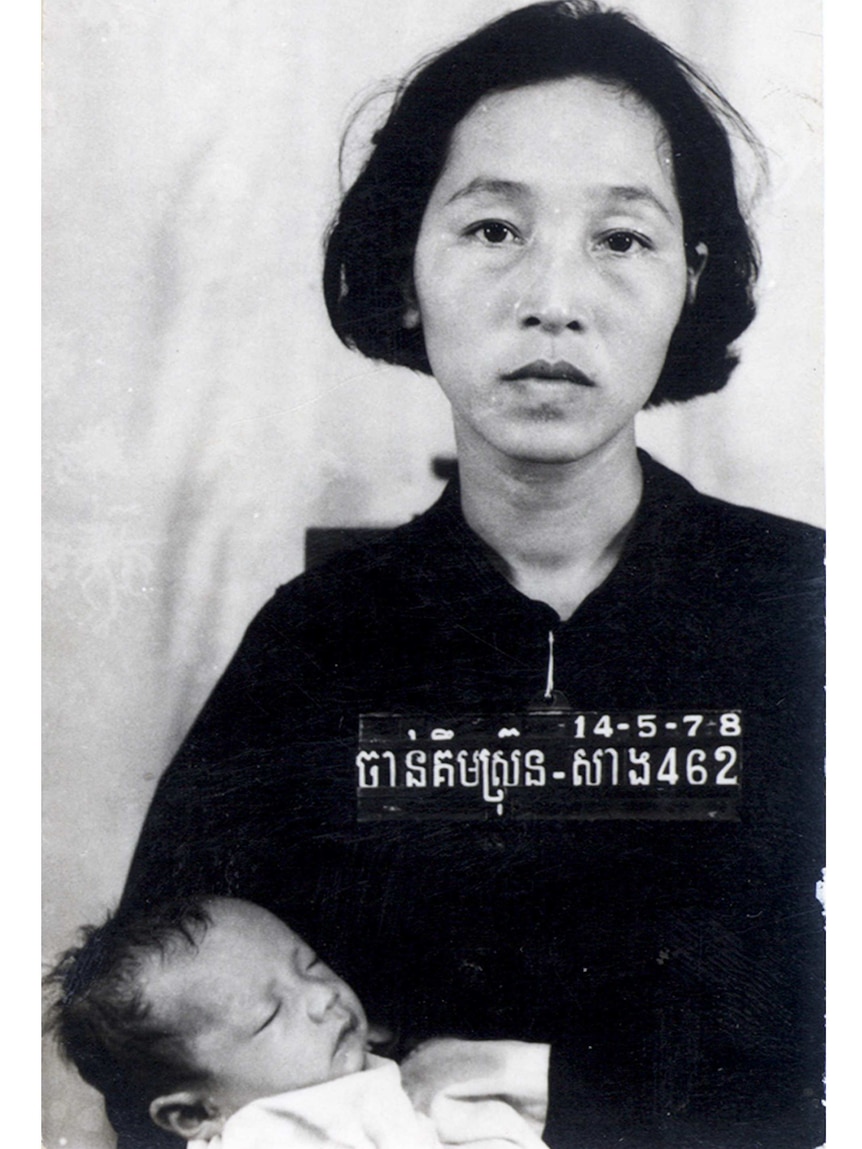 A woman of Cambodian appearance and short dark hair stares straight at the camera. She is holding a sleeping baby.