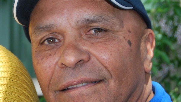 Close up photo of Derek Bromley as a middle-aged man, wearing blue cap and blue shirt, smiling.