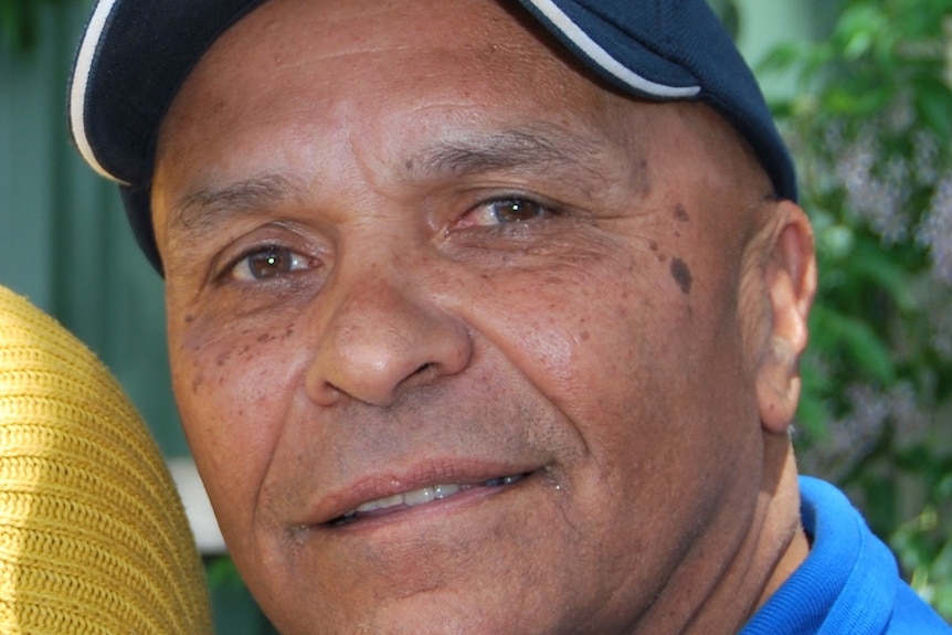Close up photo of Derek Bromley as a middle-aged man, wearing blue cap and blue shirt, smiling. 