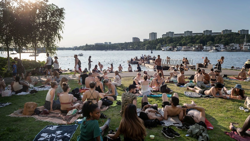 Swedes gather in the sun around a lake.