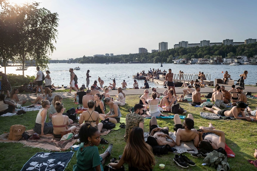 Swedes gather in the sun around a lake.