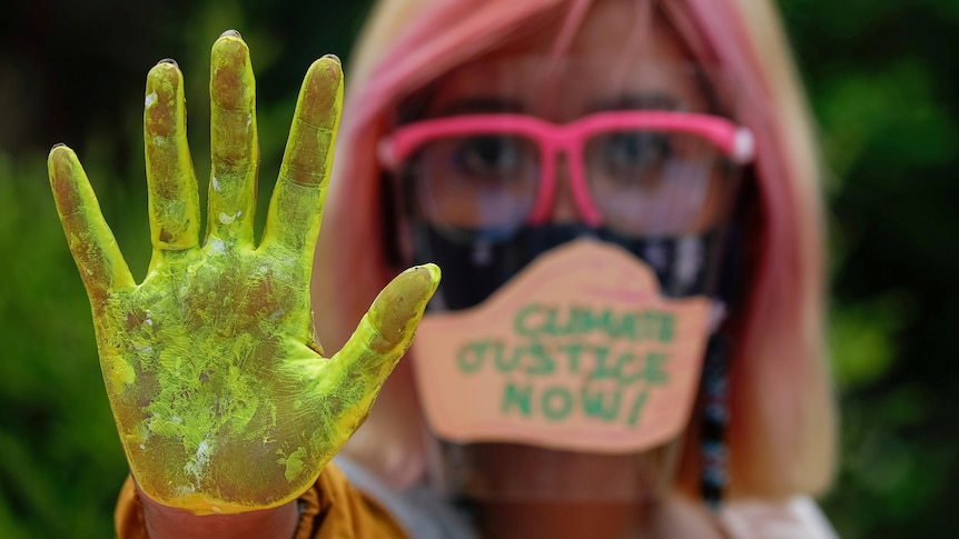 A Filipino climate activist wearing a face shield with the words "Climate Justice Now" poses showing her hand.