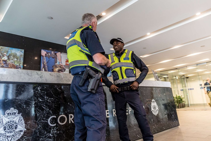 Constable Iglay Dangassat talking to an officer in front of a desk in the lobby of Victoria Police.