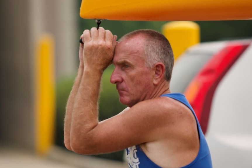 A man holds onto a rope and leans his head on his hands, looking tired and concerned.