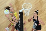 Two female netball players jump for the ball under the net, with another player to the side