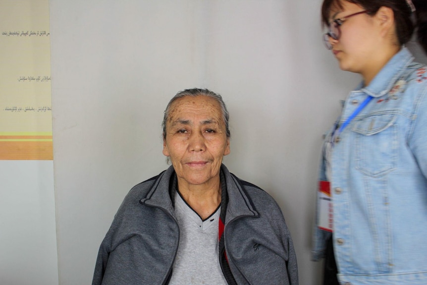 A woman in a police mugshot with another woman blurry beside her.