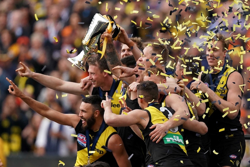 Richmond Tigers players lift the premiership trophy and point forward
