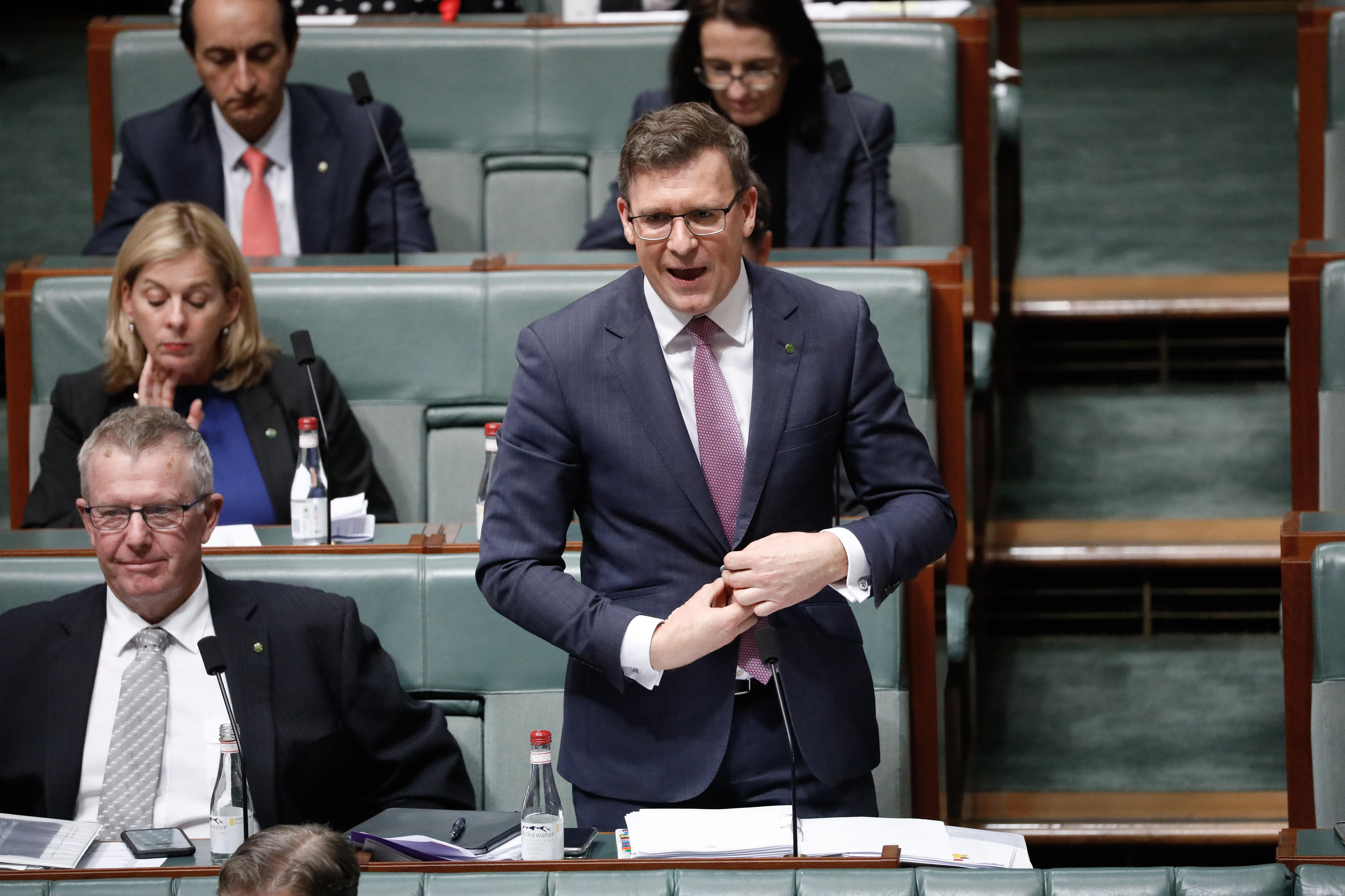 Tudge is standing, doing up a jacket button and speaking with colleagues nearby.
