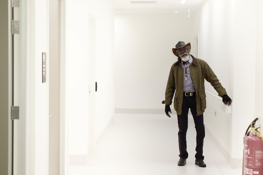 Actor David Gulpilil, an older Yolngu man standing in a hospital corridoor, in the documentary My Name is Gulpilil