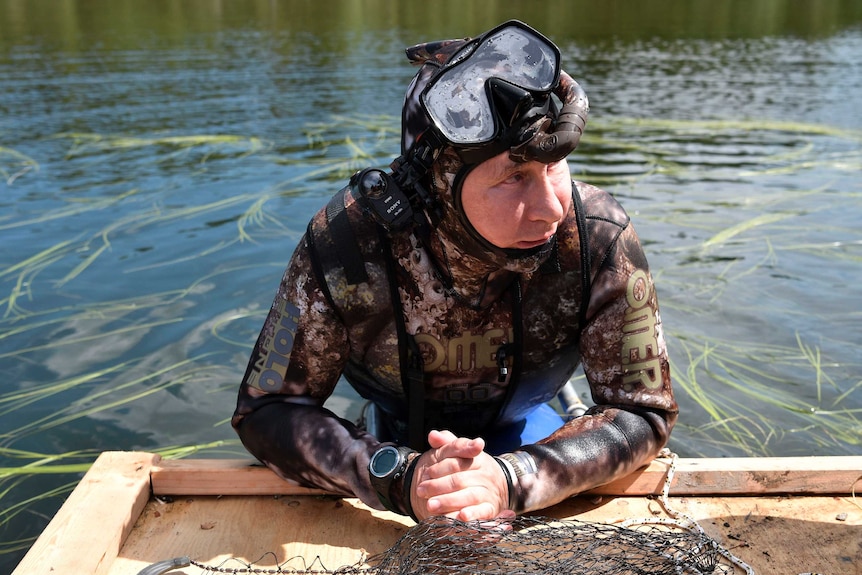 Vladimir Putin rests on a dock while wearing a snorkel and wetsuit.