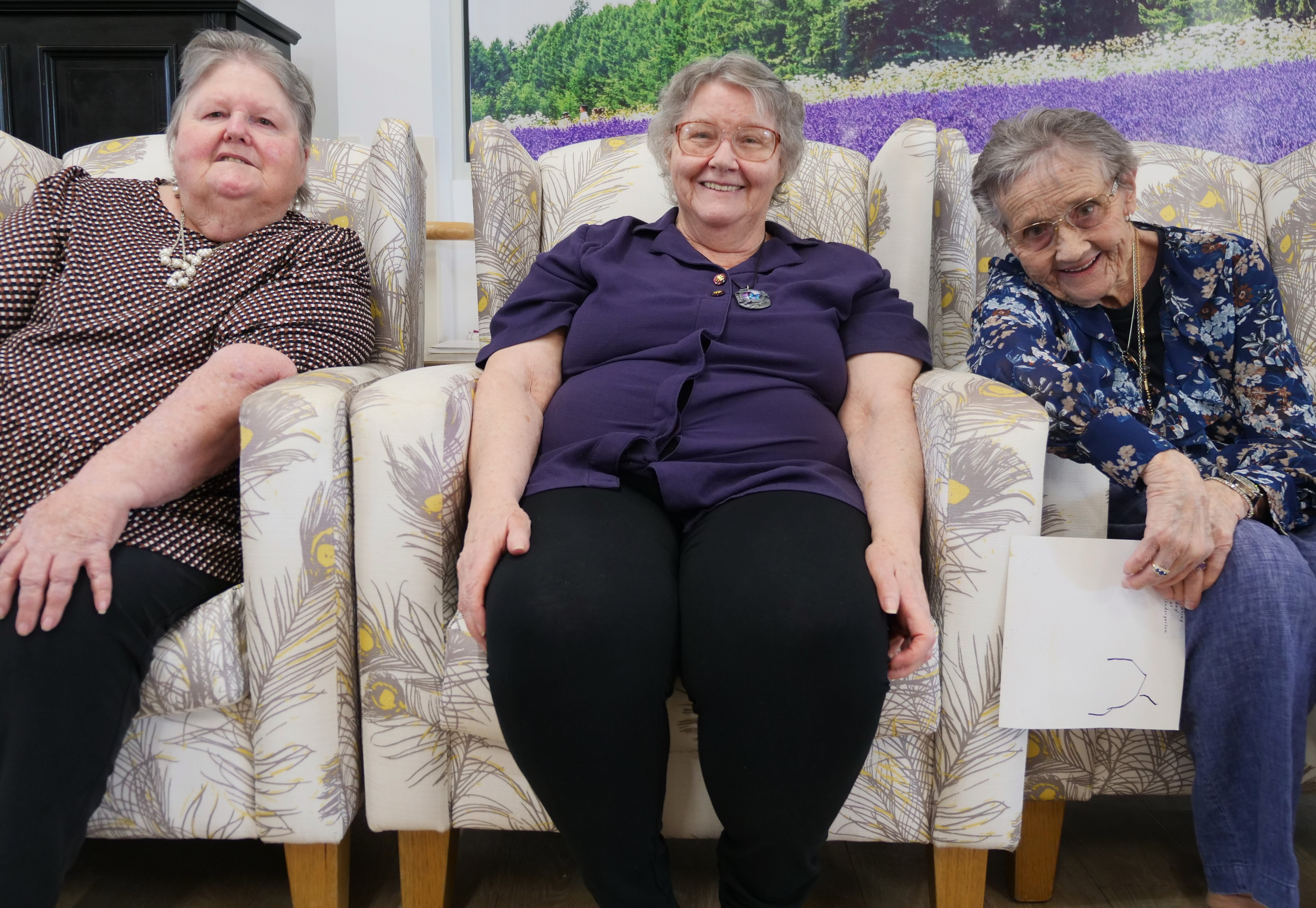 The elderly women sit in armchairs in a row