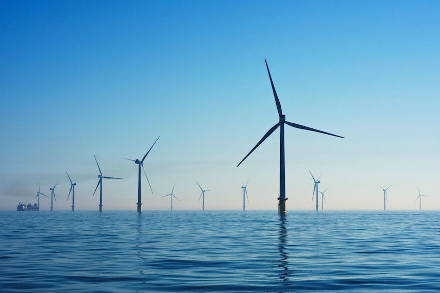 An impression of large white wind turbines in the ocean