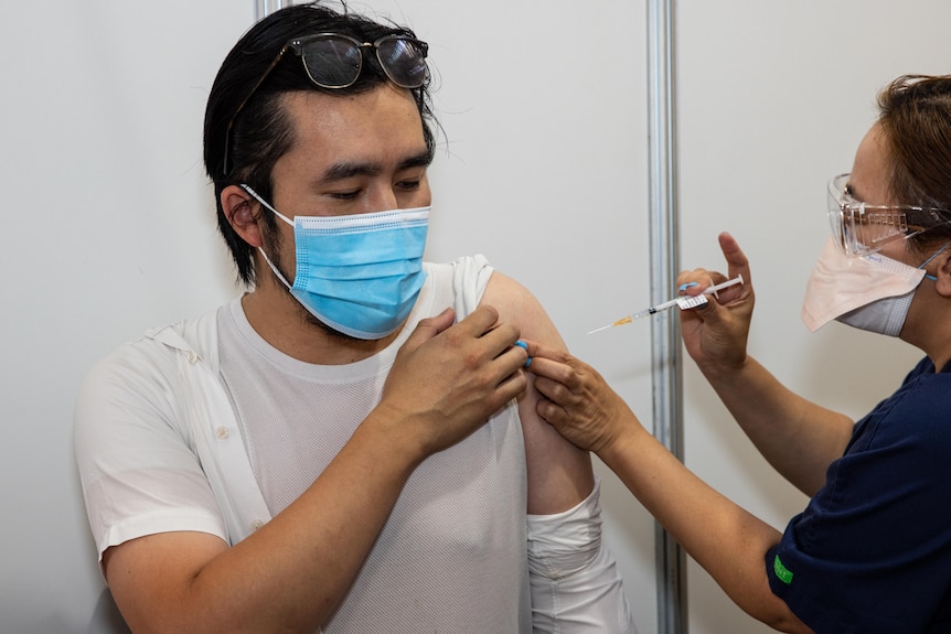 A man wearing a mask gets a needle in his upper arm.