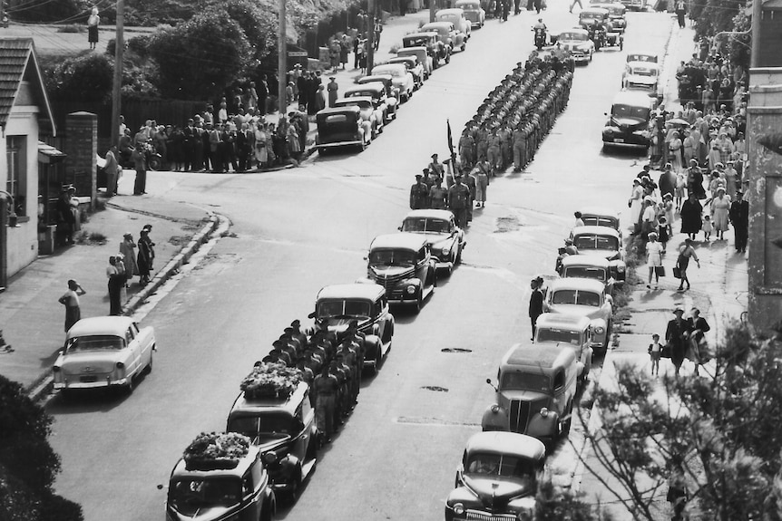 A convoy and crowds gathered along a street for a funeral.