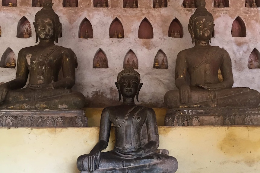 Three Buddhist statues on a temple in Laos.