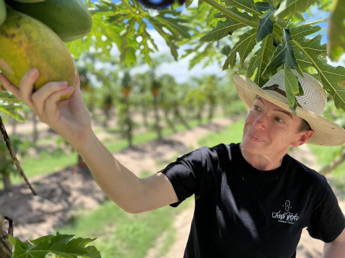 A woman in a black t-shirt and white hat holds a papaya fruit