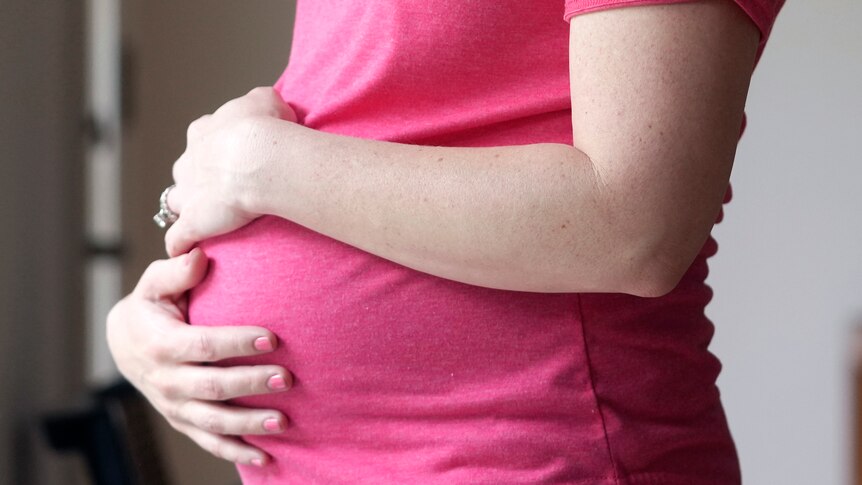 A close-up of a woman wearing a t-shirt, wrapping her arms around her pregnant belly