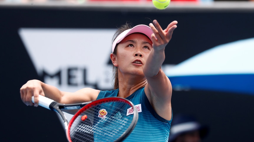 A woman looks at a tennis ball as she throws it 