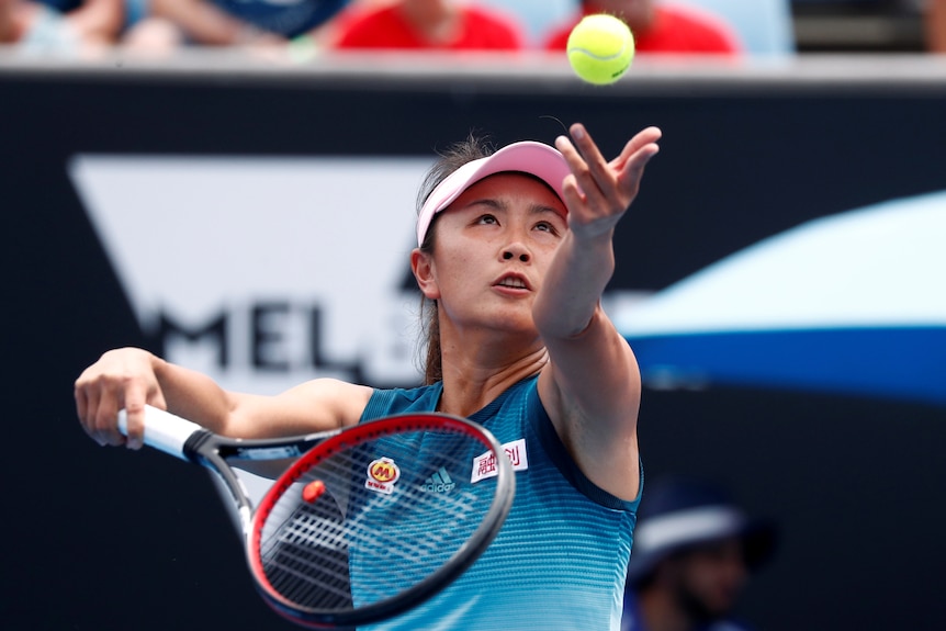 A woman looks at a tennis ball as she throws it 