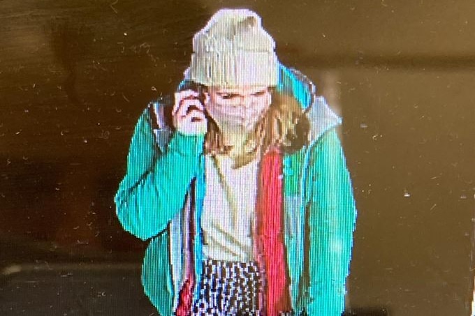 Une capture d'écran d'une femme portant un bonnet, un masque facial et un manteau vert marchant tout en parlant au téléphone