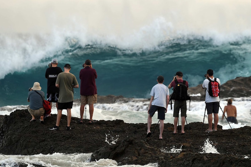Photographers are seen at Snapper Rocks on the Gold Coast with a large wave behind them.