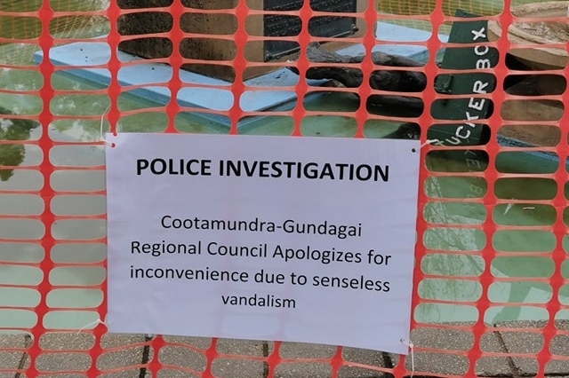 A temporary red mesh fence is erected around the toppled fountain mounted with a sign that says 'Police investigation'.