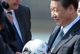 Xi Jinping smiles and holds a soccer ball while wearing a suit