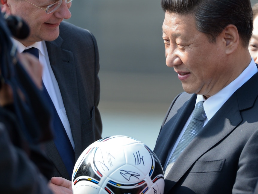 Xi Jinping smiles and holds a soccer ball while wearing a suit