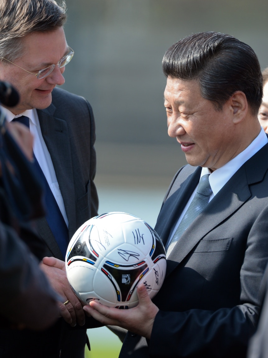 Xi Jinping smiles and holds a soccer ball while wearing a suit