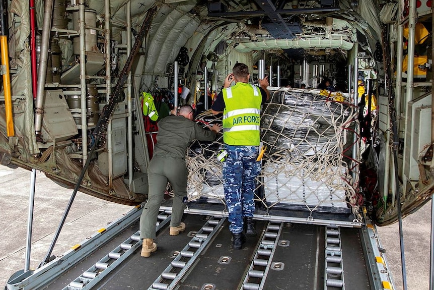 Two men push a pallet onto the back of a military plane