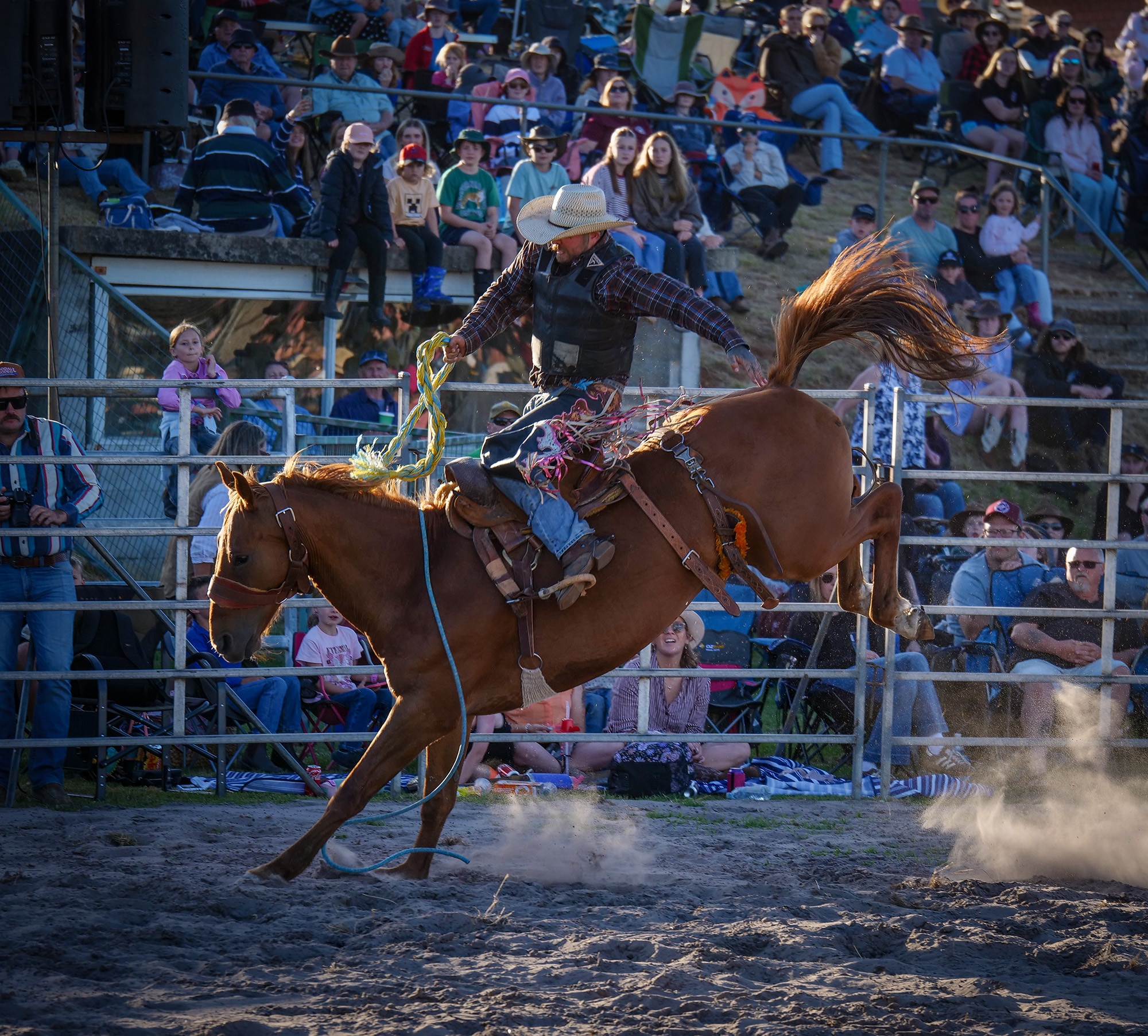 A man rides a bucking bronco in a rodeo ring
