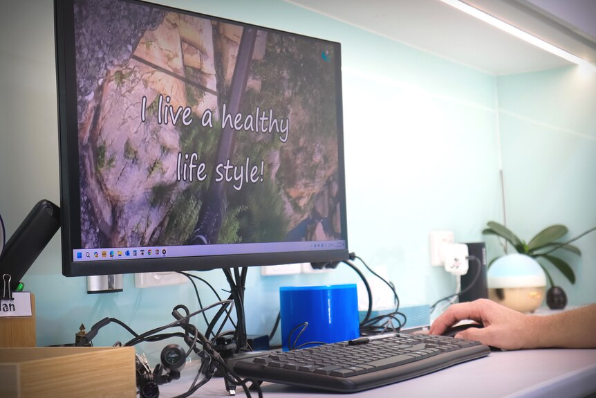 A hand on a mouse in front of a computer screen showing the words 'I live a healthy lifestyle'