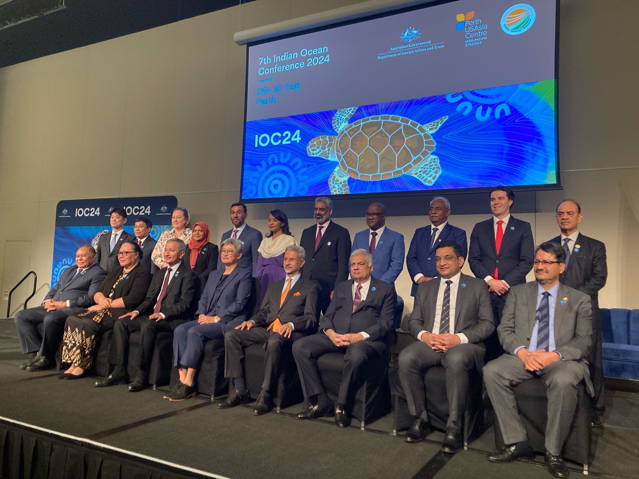Men and women wearing suits sit in two rows for a photo. 