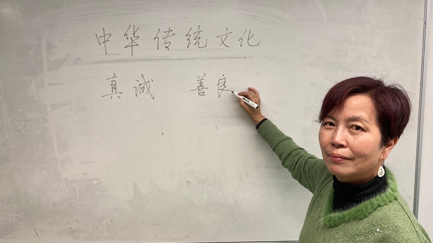 A woman stands in front of a whiteboard with Chinese on it. 